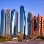 UAE, ABU DHABI, NOVEMBER, 18, 2021 - Skyscrapers surrounded by a green park of palm trees and fountains at sunset in Abu Dhabi, capital of the United Arab Emirates.